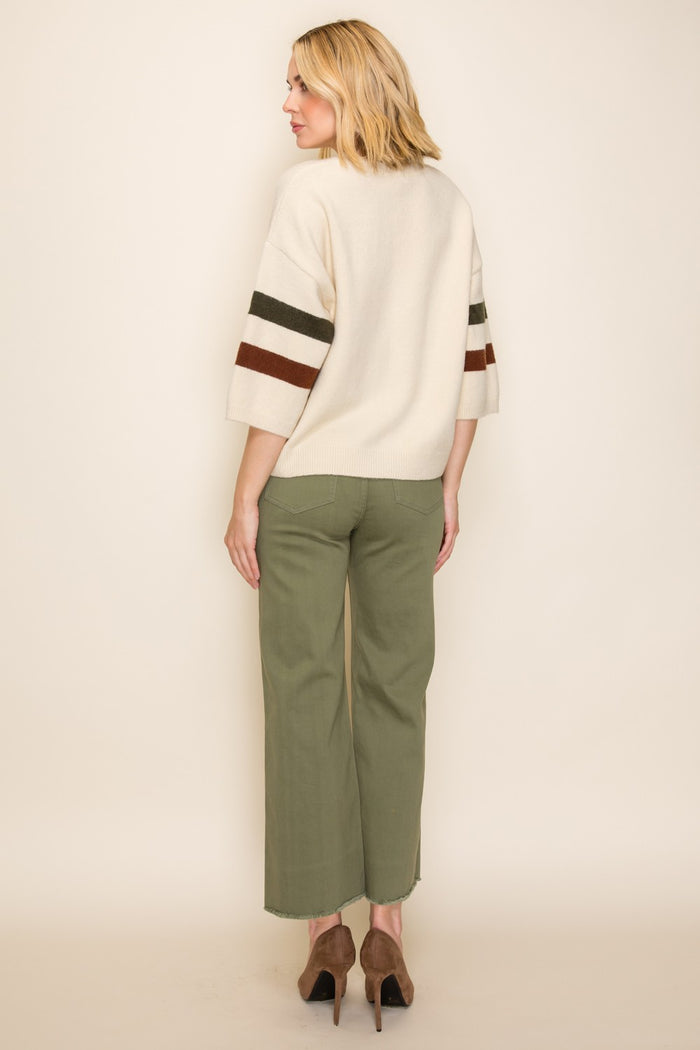 woman wearing a cream oversized sweater with brown and green stripes and olive wide-leg pants, seen from the back