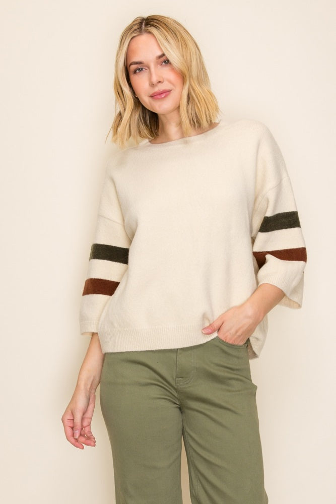 woman wearing a cream oversized sweater with green and brown striped sleeves and olive green pants