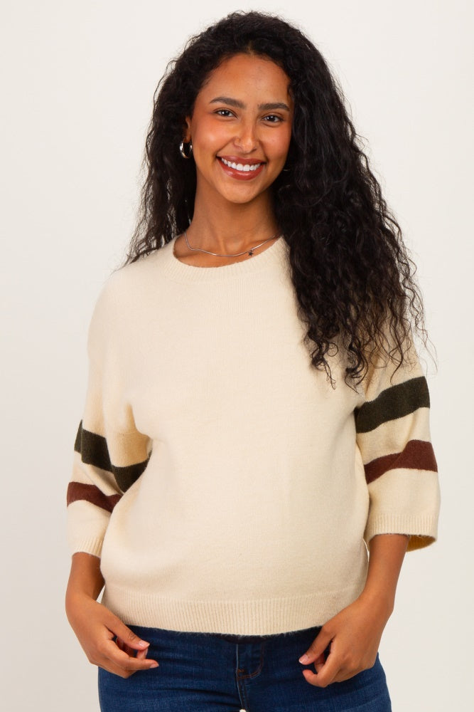 woman wearing a cream maternity sweater with striped sleeves and a visible baby bump, smiling at the camera