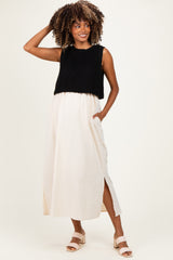 woman wearing a black knitted maternity top and a beige maxi skirt with a side slit, posing with one hand on her hip