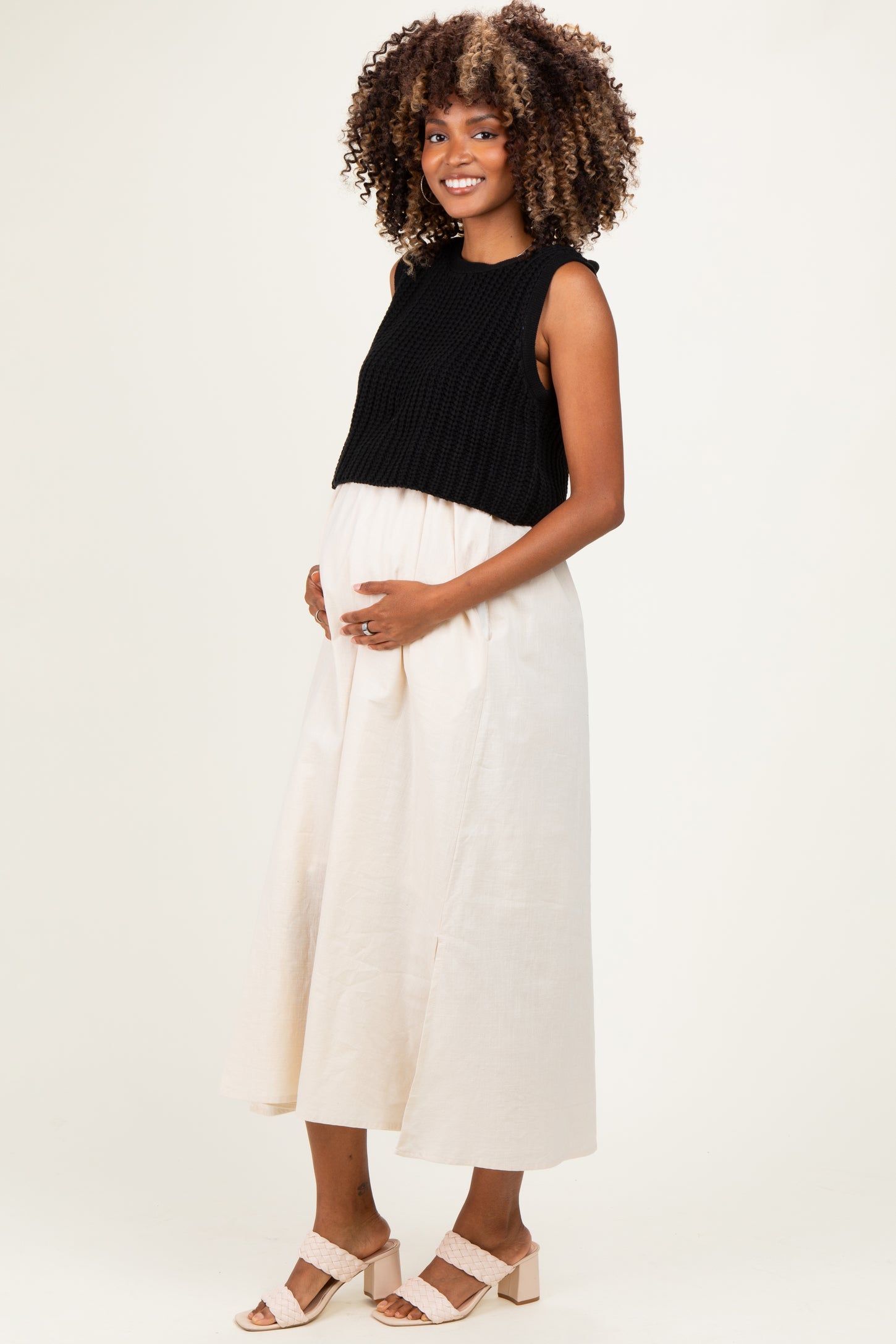 woman wearing a black sleeveless knit top and a cream midi skirt, showing her baby bump