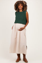 woman wearing a dark green knitted crop top and a light beige maxi skirt, showcasing her baby bump in maternity wear