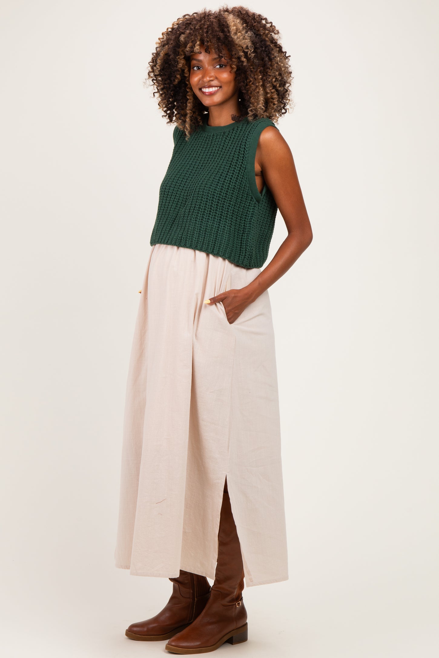 woman wearing a dark green knitted crop top and a light pink maxi skirt with pockets, showcasing her baby bump