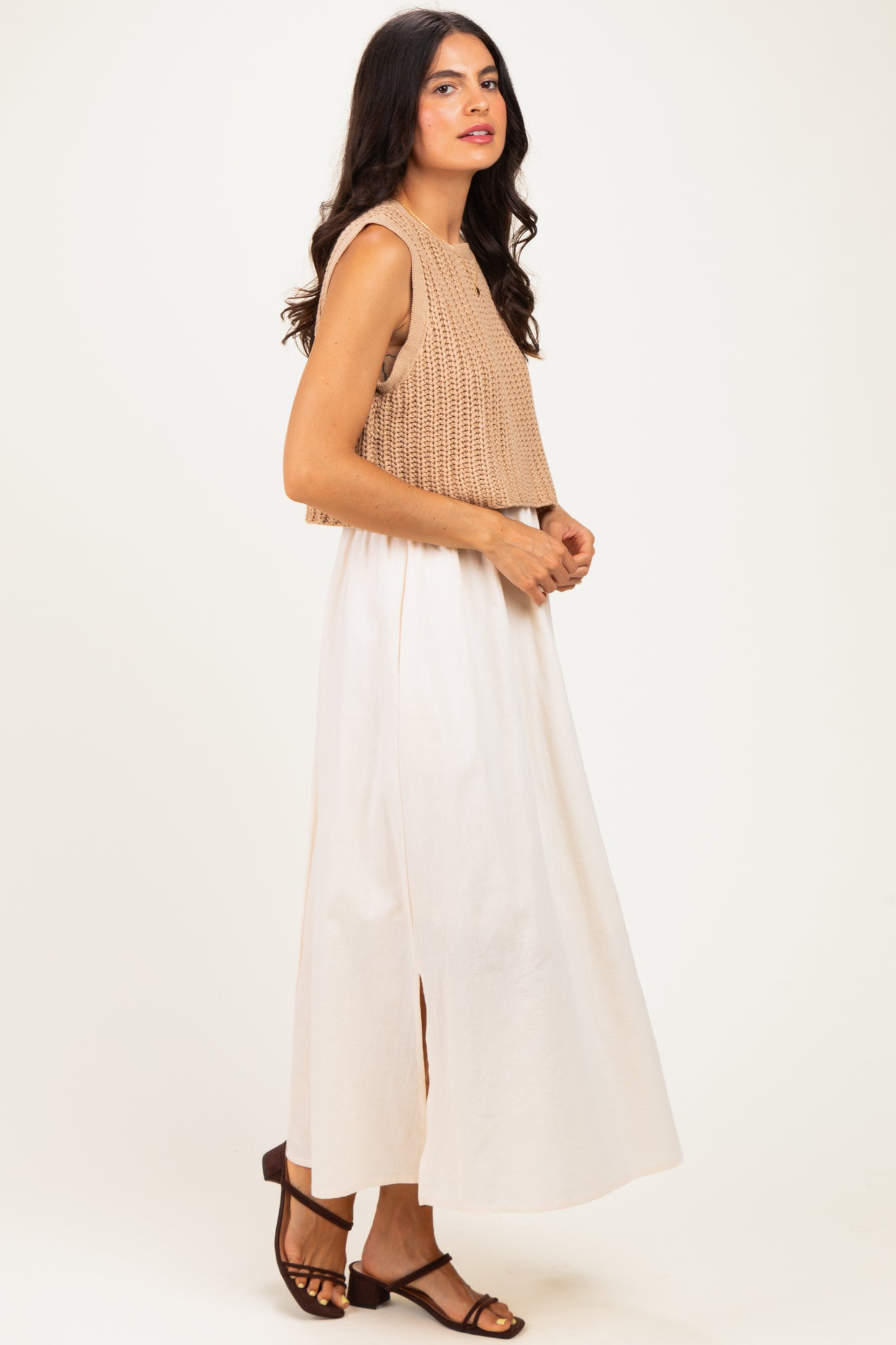 woman wearing a beige cropped knit tank top and a flowy white maxi skirt with a side slit