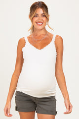 woman wearing a white maternity tank top with lace trim and holding her baby bump, paired with gray shorts