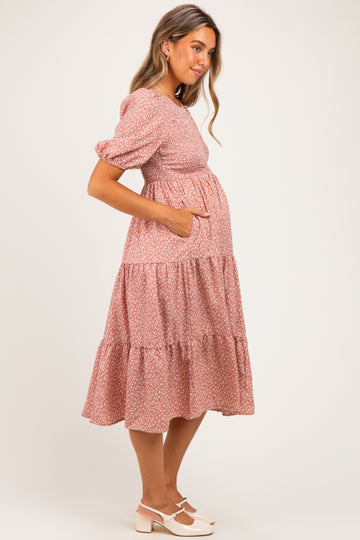 woman wearing a pink floral maternity dress with puff sleeves and a tiered skirt, showing her baby bump