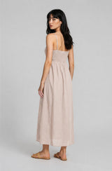woman wearing a light beige midi dress with a smocked bodice and adjustable straps, standing with her back to the camera