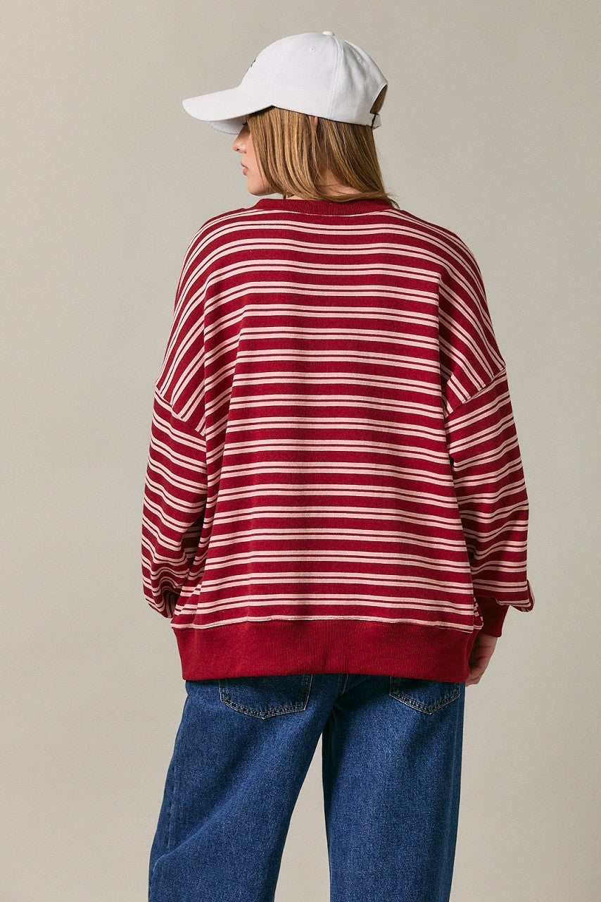 woman wearing a red and white striped oversized sweater and a white baseball cap, showing the back view