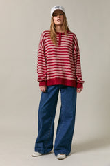 woman wearing a red striped oversized sweater with buttons and wide-leg blue jeans, styled with a white cap