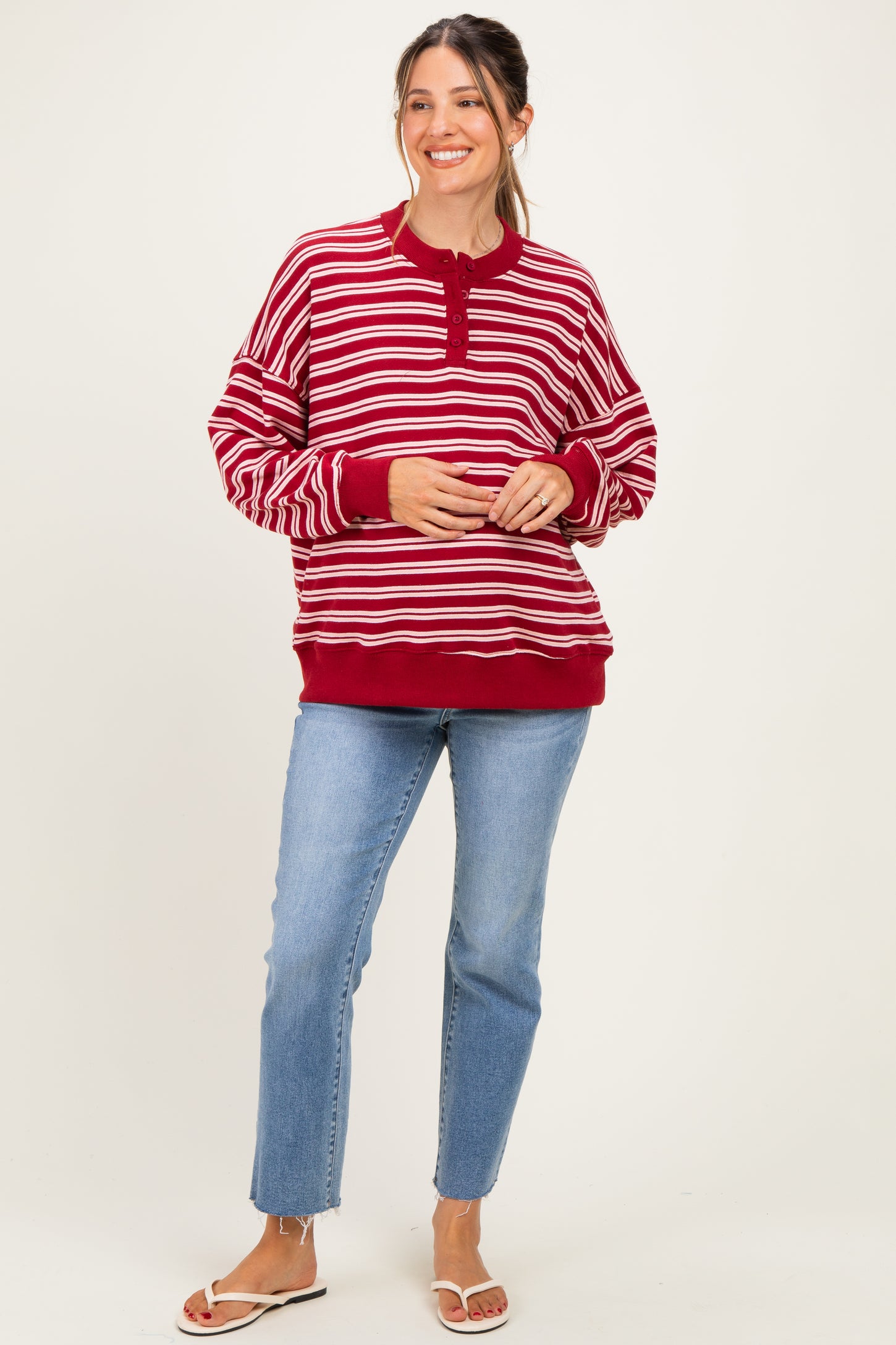 woman wearing a red and white striped maternity sweatshirt with a button front and relaxed fit, paired with light blue jeans