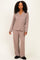 woman wearing a taupe long sleeve pajama set with white piping and matching pants, standing against a neutral background