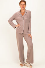 woman wearing a taupe long sleeve pajama set with white piping and wide-leg pants, standing on a light background