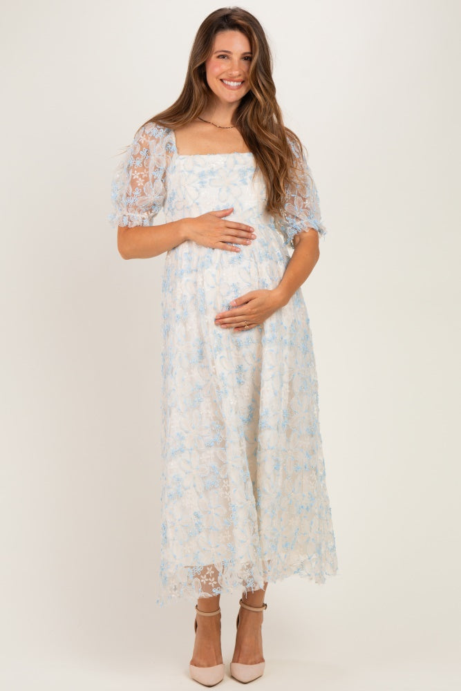 woman wearing a light blue floral lace maternity dress and showing her baby bump