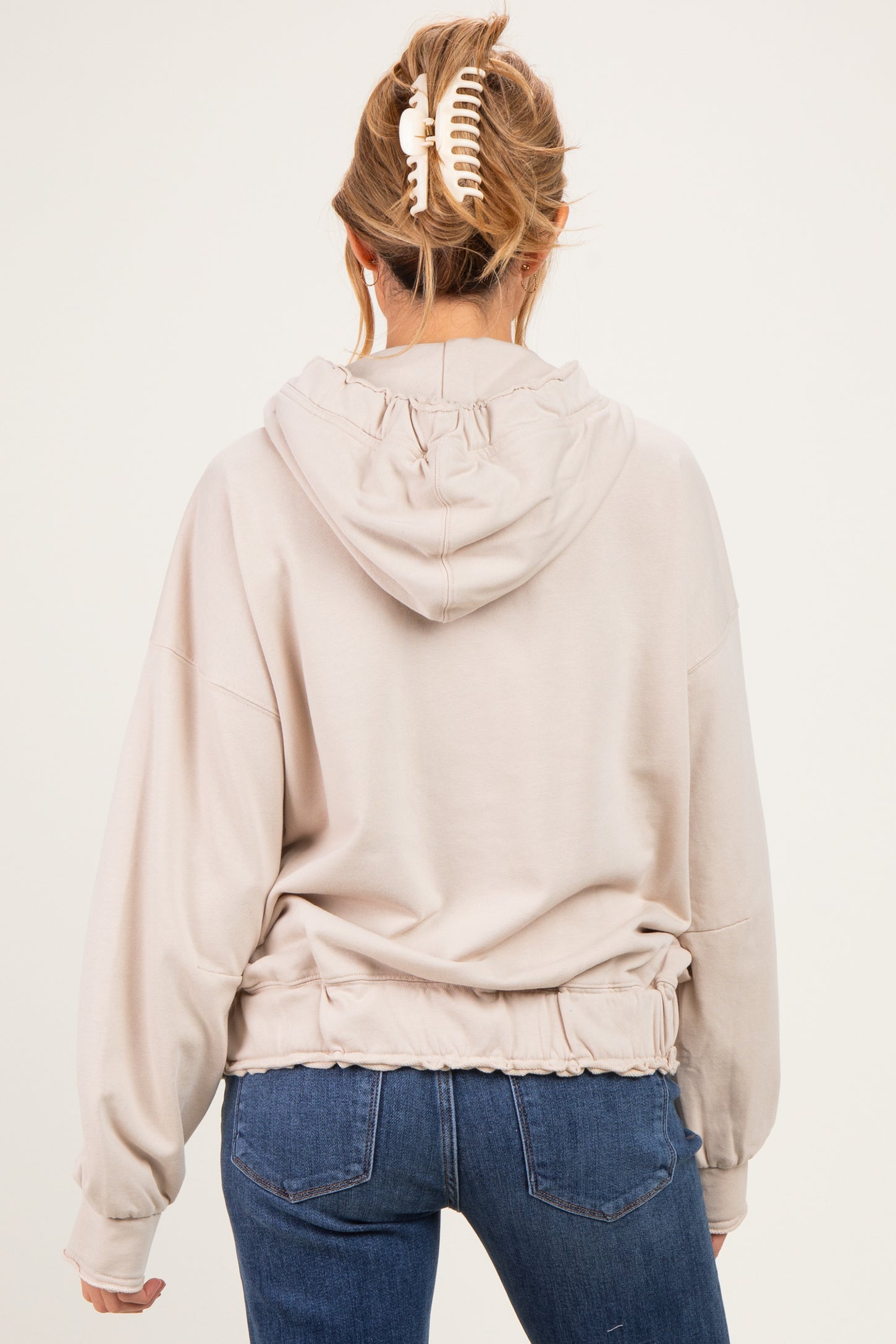 woman wearing a beige maternity hoodie with a cinched waist and hood, seen from the back
