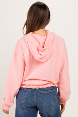 woman wearing a light pink maternity hoodie with a cinched bottom and hood, showing the back view