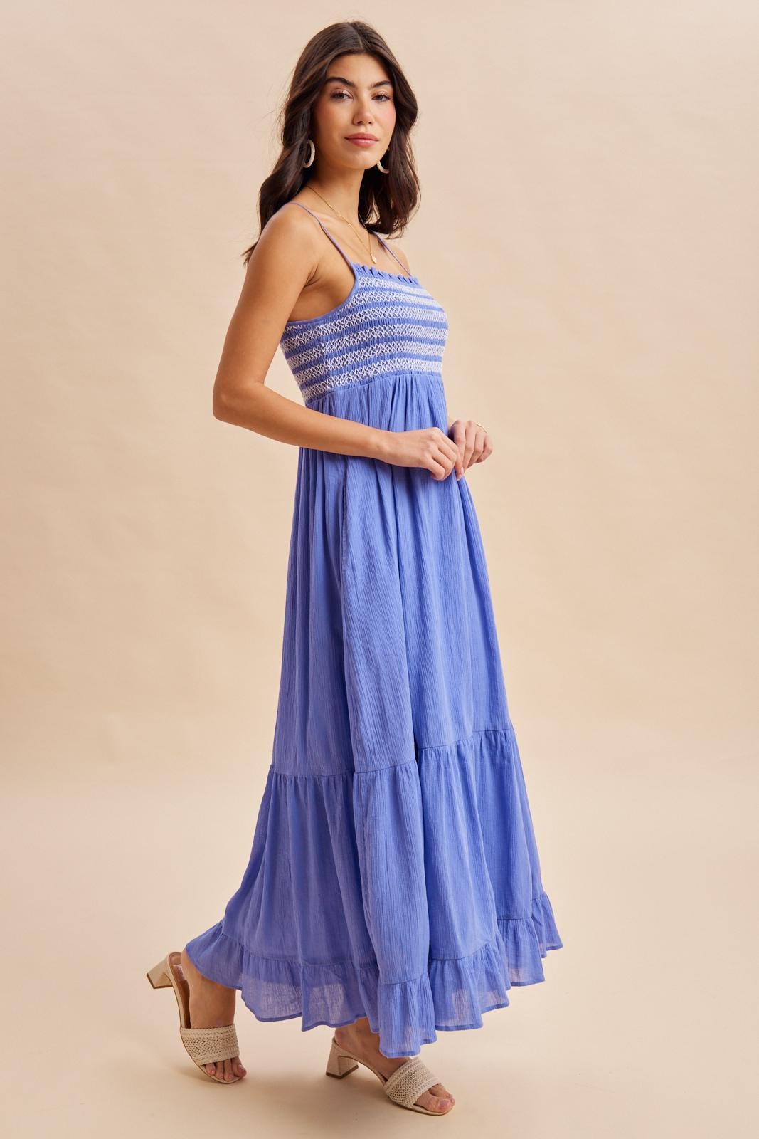 woman wearing a blue maxi dress with a smocked bodice and tiered skirt, standing on a neutral background