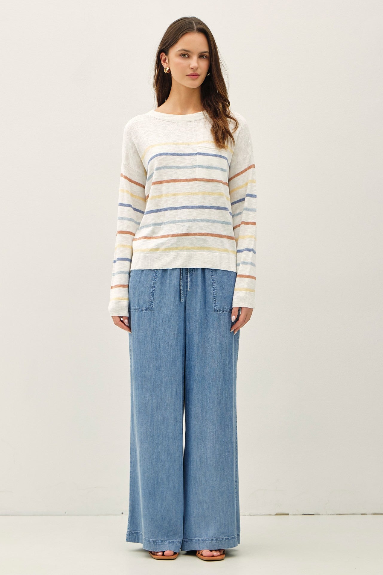 woman wearing a cream striped sweater with a pocket and light blue wide-leg pants
