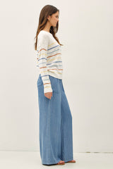 woman wearing a cream striped sweater and wide-leg blue denim pants, standing in profile against a white background