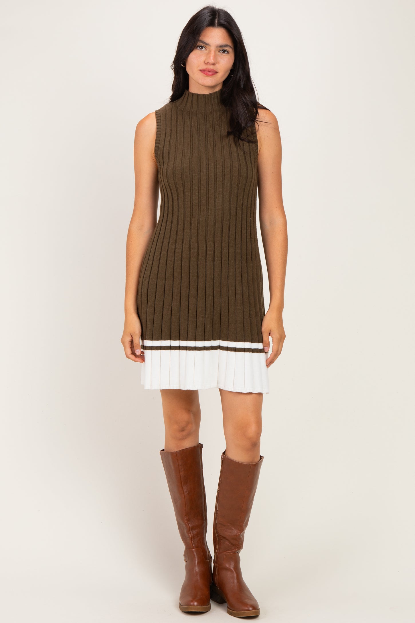 woman wearing an olive green ribbed knit sleeveless dress with a white pleated skirt and knee-high brown boots