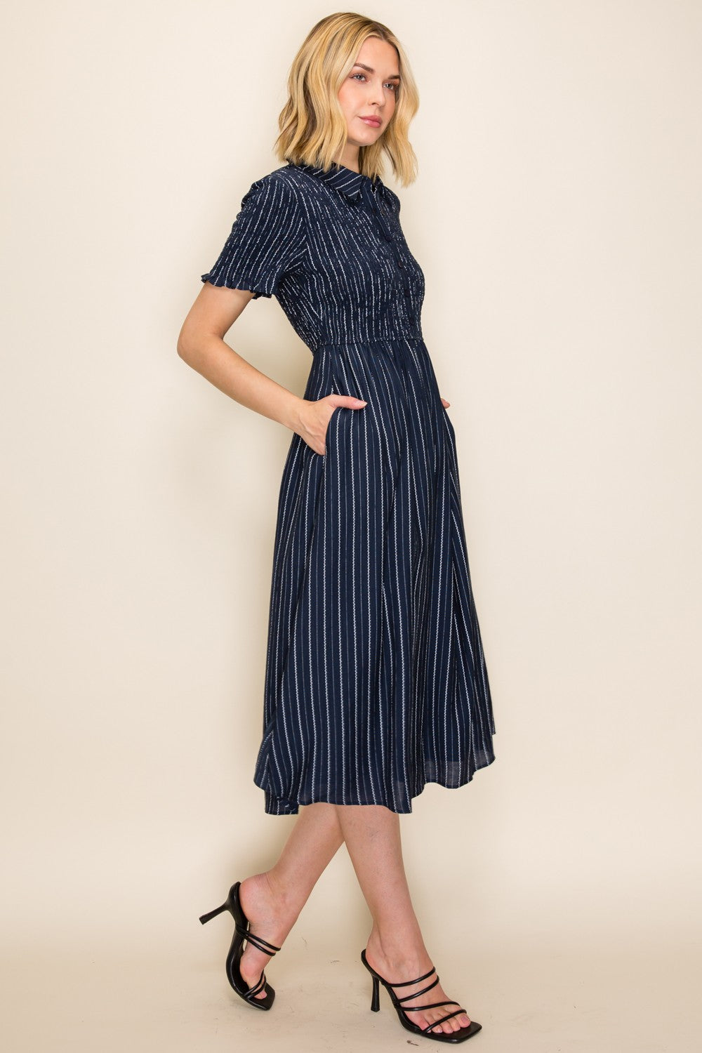 woman wearing a navy blue striped button-up midi dress with a cinched waist and pockets, paired with strappy black heels