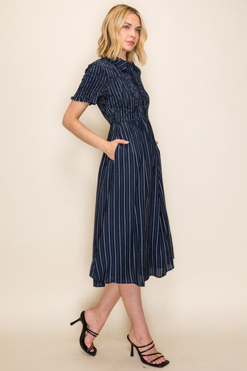 woman wearing a navy blue striped button-up midi dress with a cinched waist and pockets, paired with strappy black heels