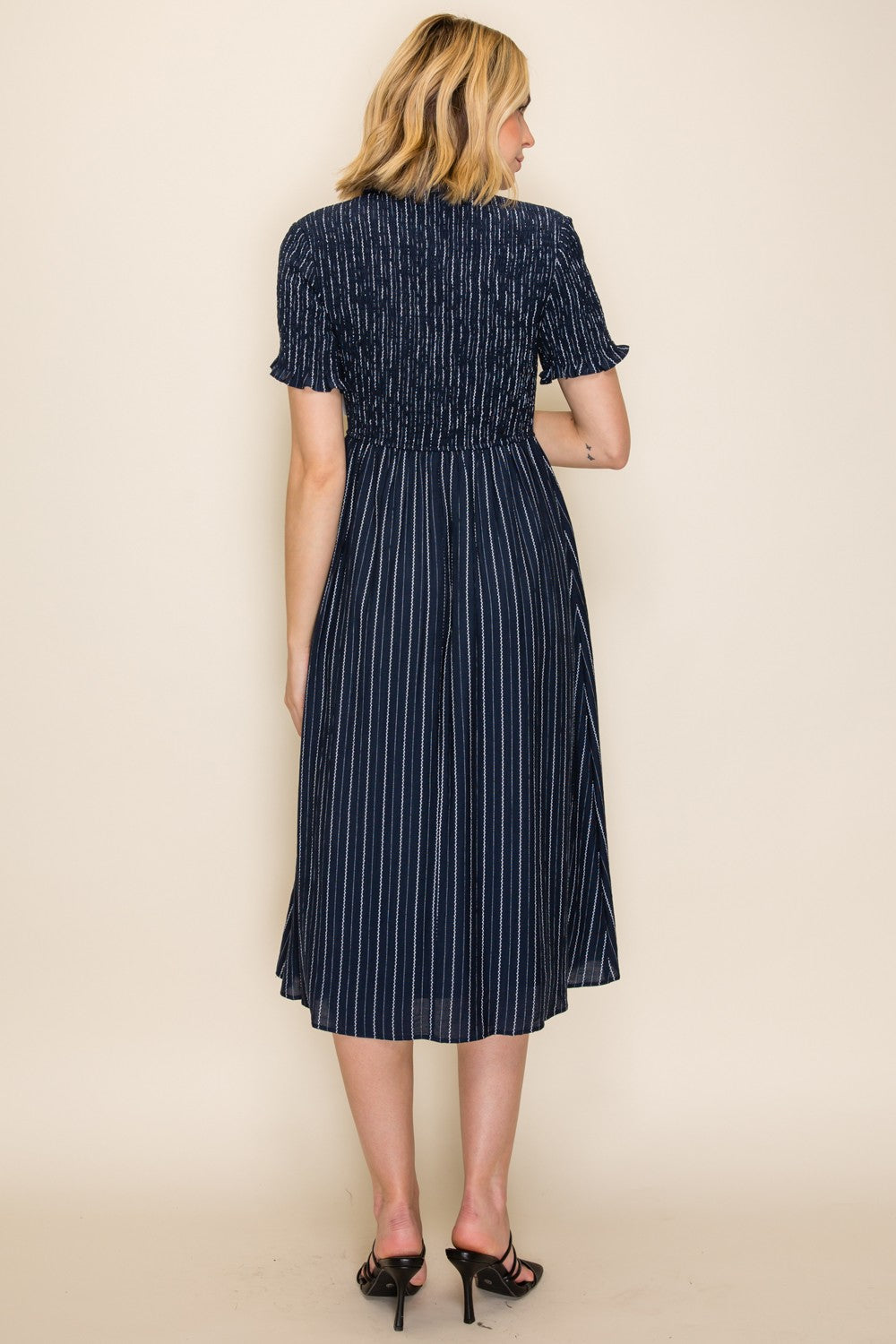 woman wearing a navy blue midi dress with vertical stripes and smocked back detail, viewed from the back