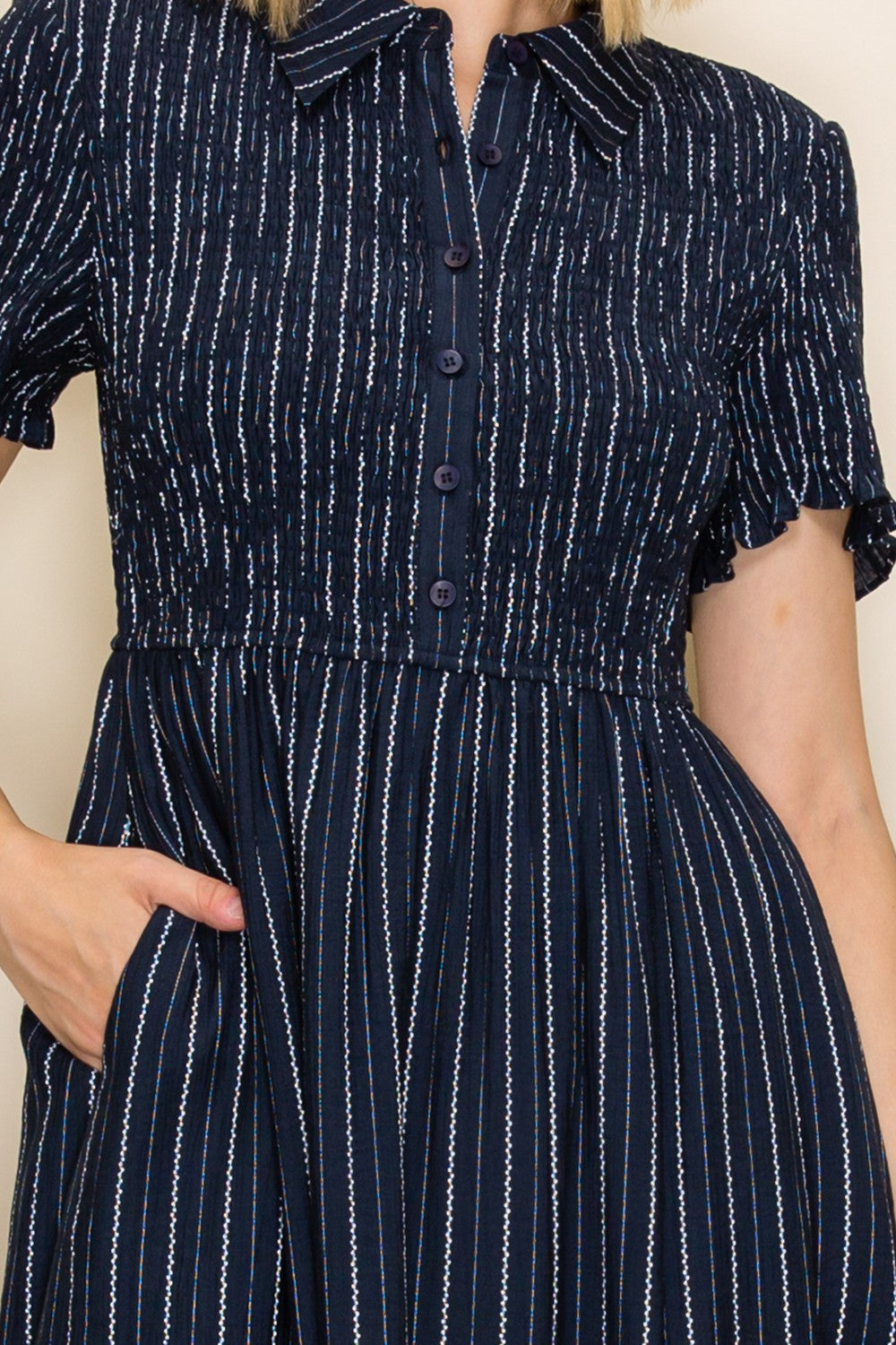 woman wearing a navy blue button-up dress with a smocked bodice and short sleeves, featuring vertical stripes and pockets