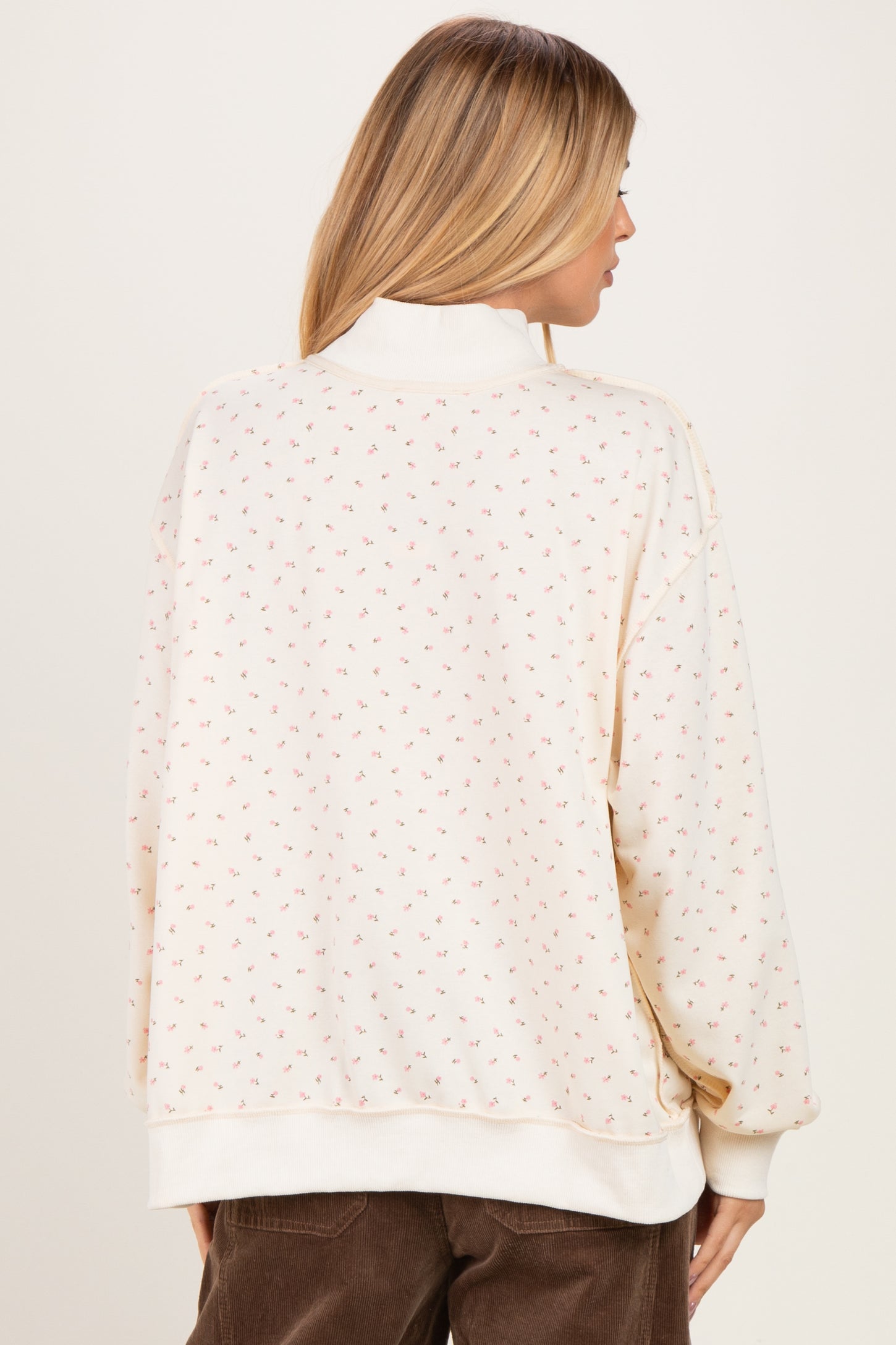 woman wearing a cream sweater with a small floral pattern and high neckline, viewed from the back