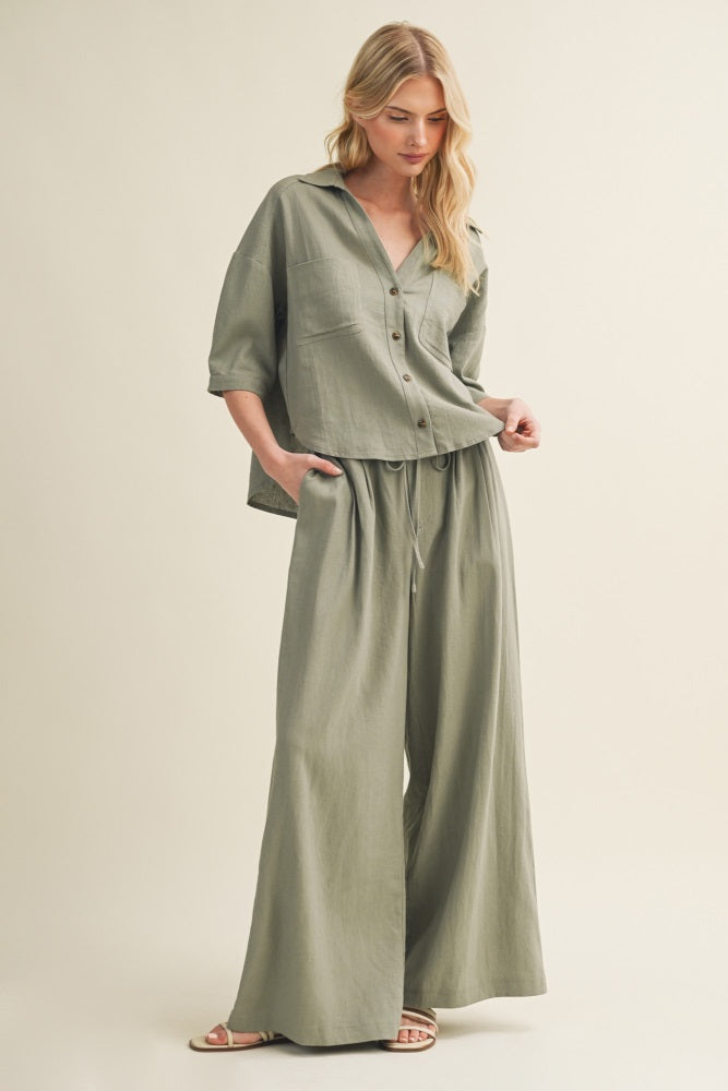 woman wearing a relaxed fit olive green two-piece outfit with a button-up top and wide leg pants