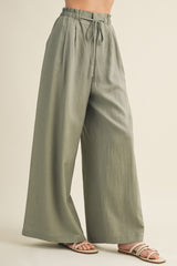 woman wearing light green wide-leg pants with a drawstring waist and side pockets, paired with strappy sandals
