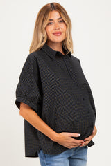 woman wearing a black and blue checkered maternity shirt with a button-down style and holding her baby bump