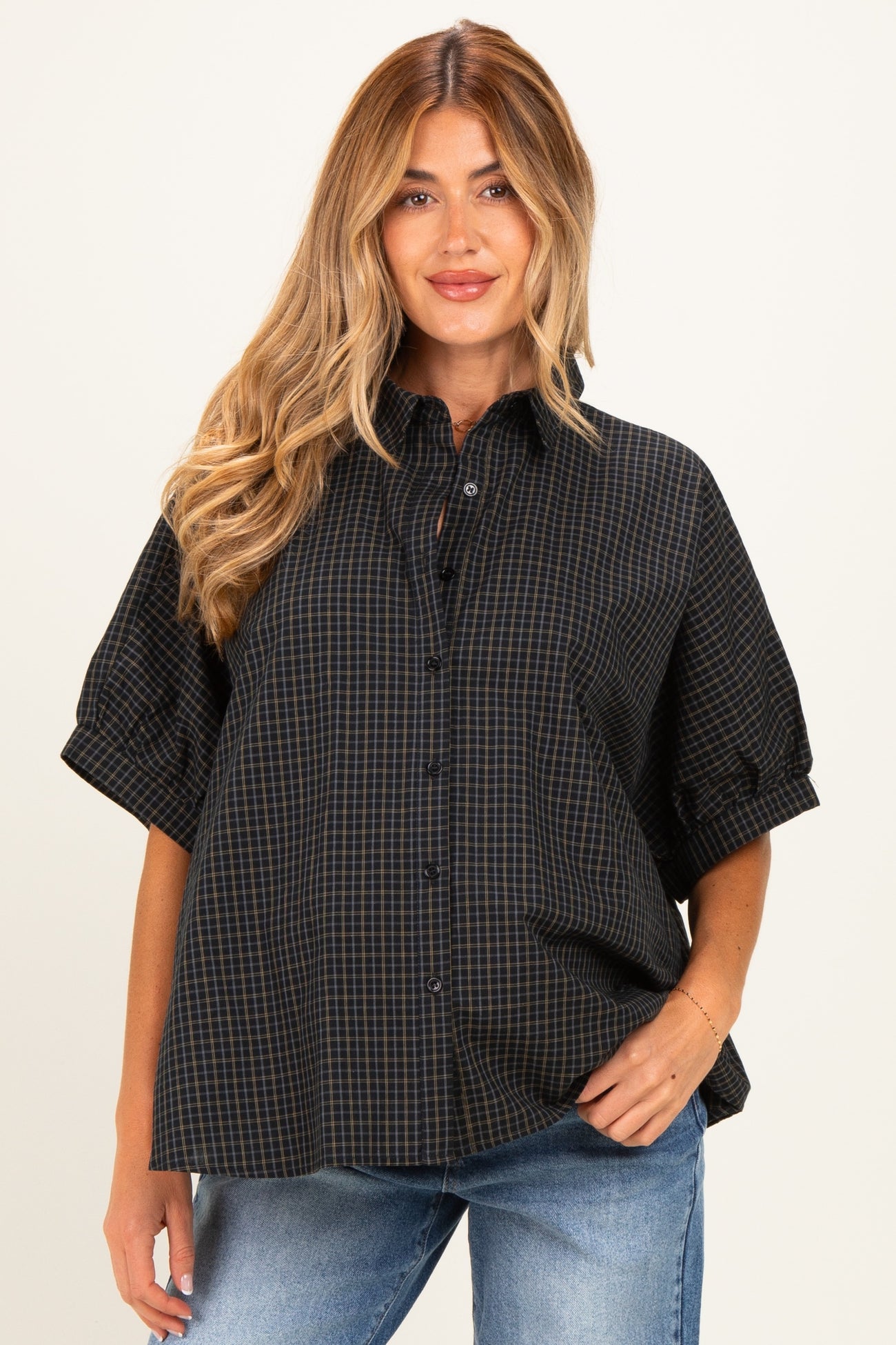 woman wearing a black and navy checkered maternity shirt with short sleeves and button detail, smiling at the camera