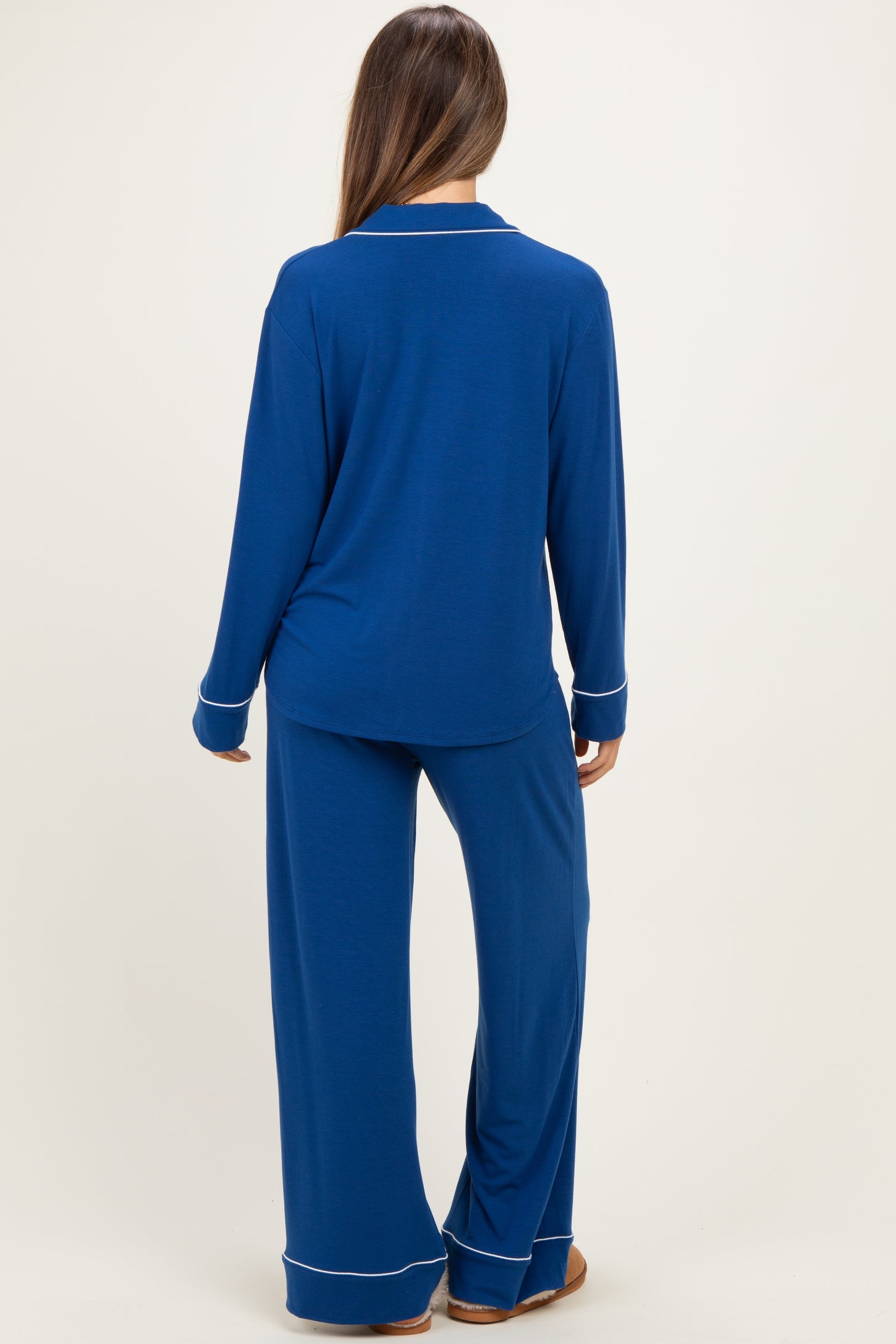 woman wearing a long-sleeve maternity pajama set in navy blue with white trim, viewed from the back