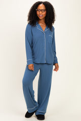 woman wearing a blue pajamas set with long sleeves, a pocket, and white piping details, styled with black slippers