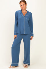 woman wearing a blue pajama set with long sleeves, pants, and white piping details, standing against a plain background