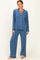 woman wearing a blue pajama set with long sleeves, pants, and white piping details, standing against a plain background
