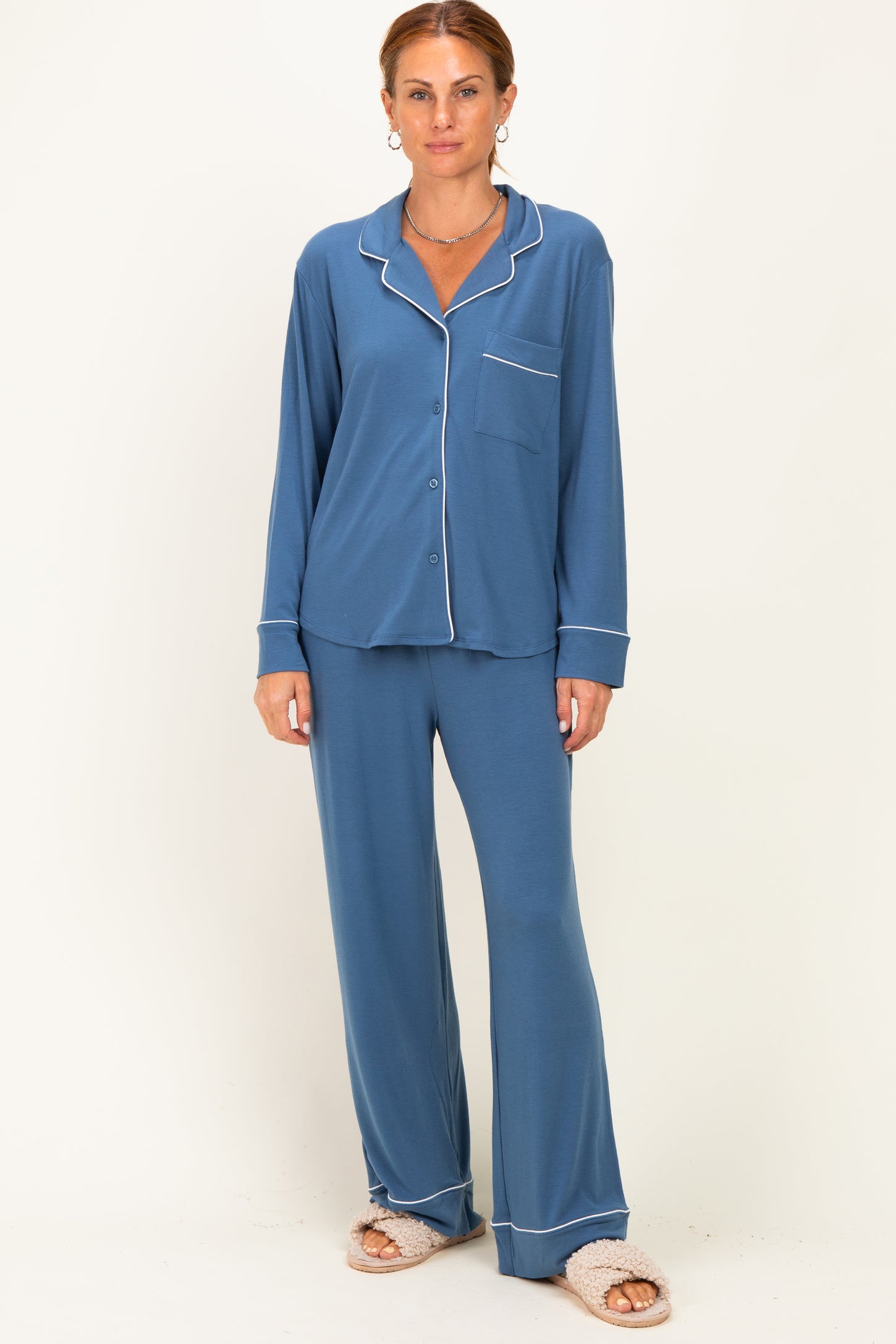 woman wearing a blue loungewear set with long sleeves and pants, featuring white piping details and fluffy slippers