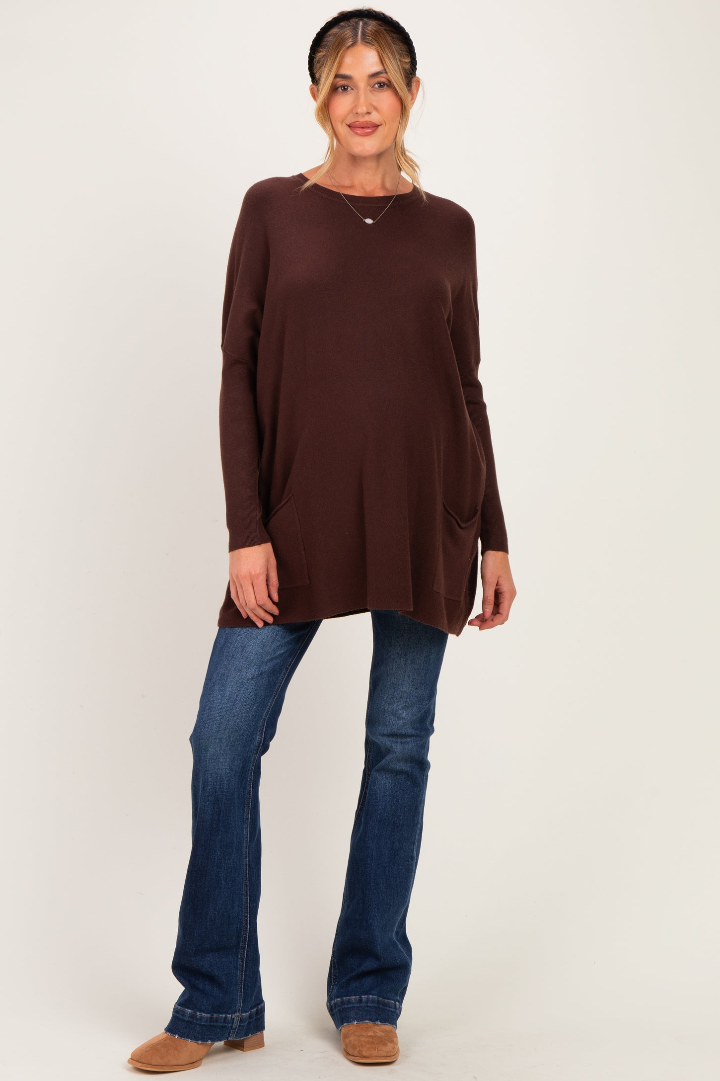 woman wearing a brown maternity tunic top with side pockets and paired with flared jeans