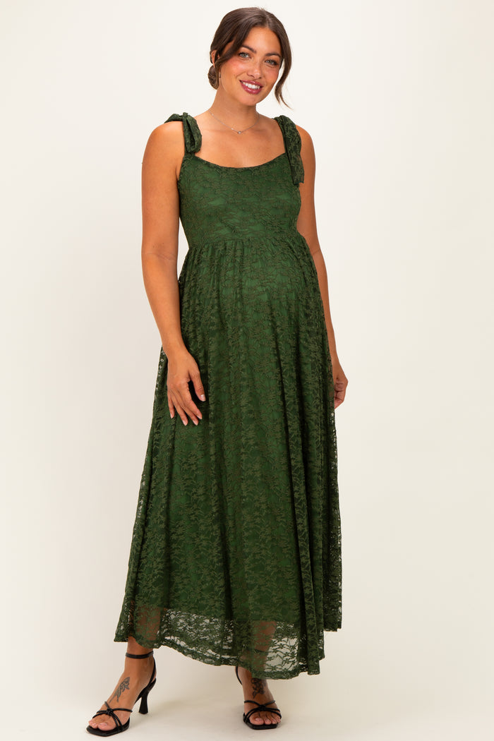 woman wearing a dark green lace maternity maxi dress with bow details on the straps and a visible baby bump