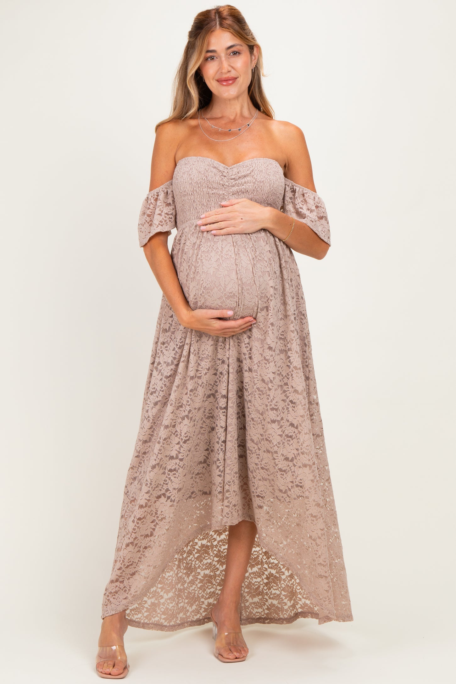 woman wearing a beige off-the-shoulder lace maternity dress and holding her baby bump