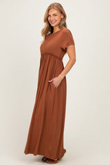 woman wearing a rust-colored maxi dress with short sleeves and pockets, smiling against a neutral background