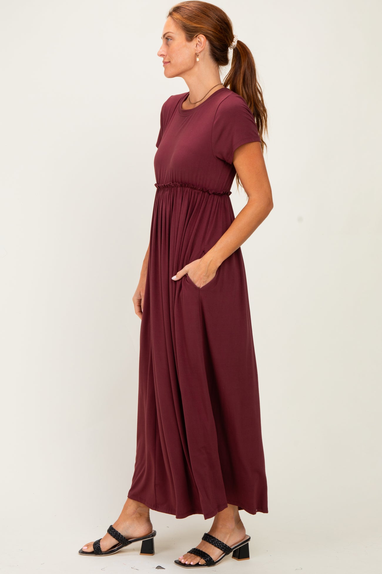 woman wearing a burgundy short sleeve maxi dress with an elastic waist and pockets, paired with black strappy sandals