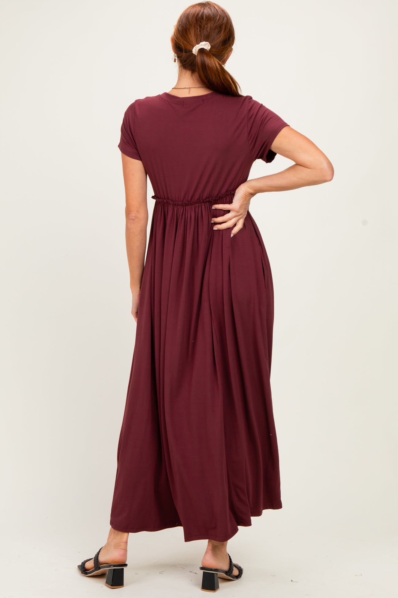 woman wearing a burgundy maxi dress with short sleeves and a gathered waistband, standing with her back to the camera