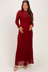 woman wearing a long-sleeve burgundy lace maternity dress and gently holding her baby bump