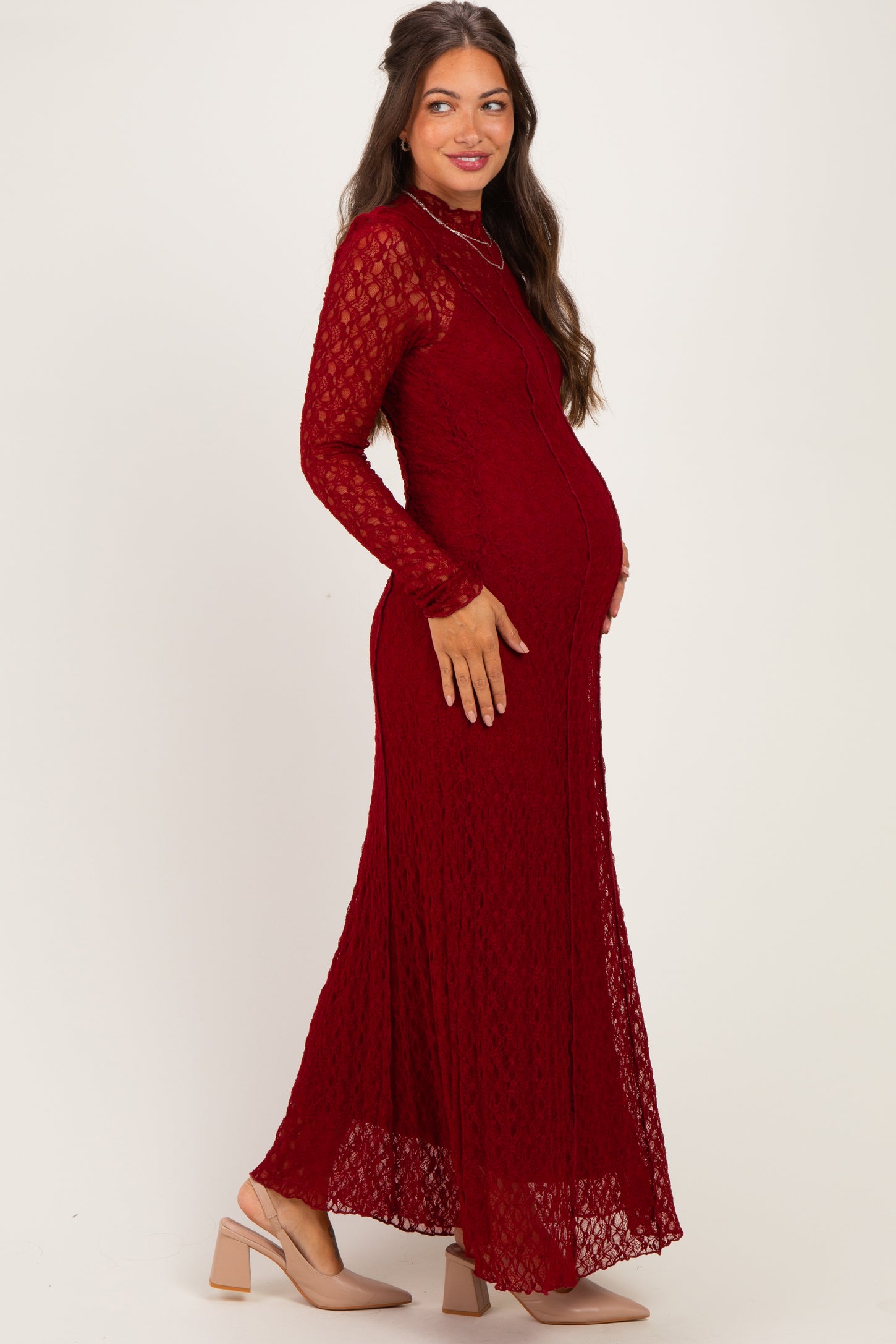 woman wearing a burgundy lace maternity dress with long sleeves and a flowing skirt, showing her baby bump