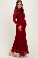 woman wearing a burgundy lace maternity dress with long sleeves and a flowing skirt, showing her baby bump