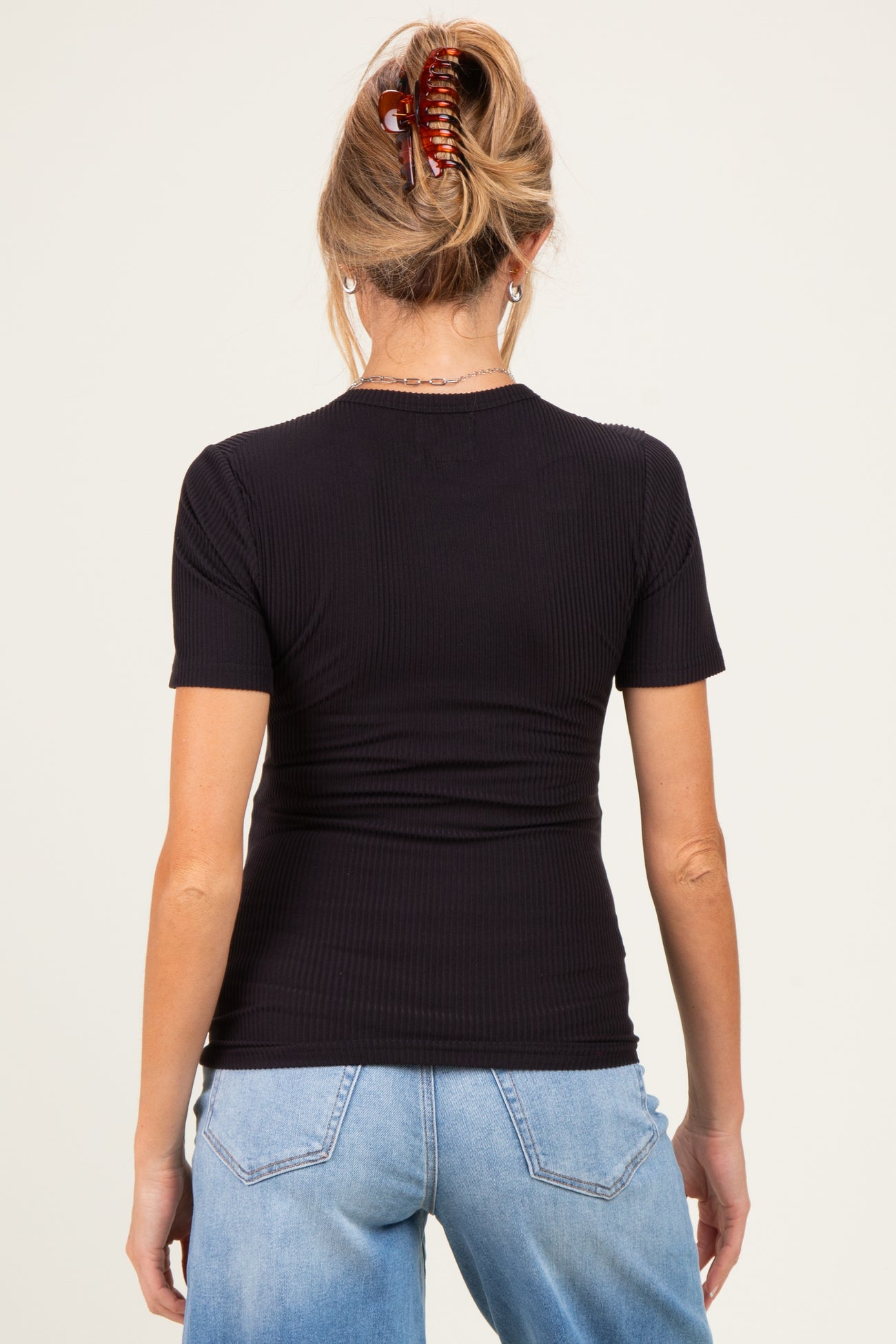 woman wearing a black ribbed short sleeve maternity top, viewed from the back with hair styled in a clip