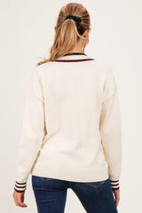 woman wearing a cream-colored maternity sweater with maroon and navy striped detailing on the collar and cuffs