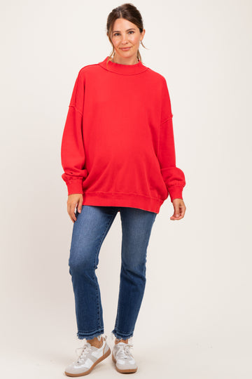 woman wearing a red oversized maternity sweatshirt and blue jeans showing her baby bump