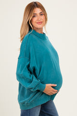 woman wearing a teal oversized maternity sweatshirt and holding her baby bump
